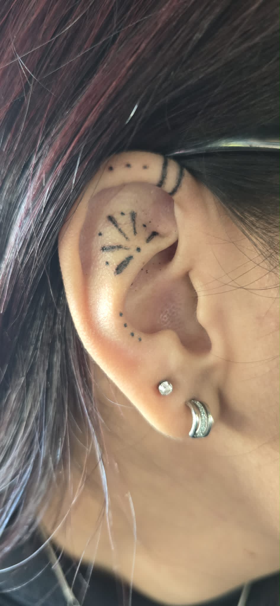 Minimalist black work ear tattoo with sunburst design
